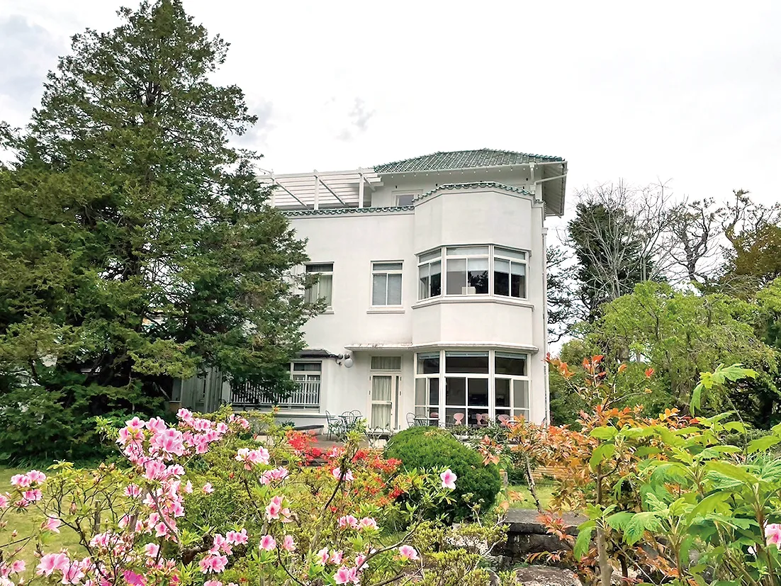 小田原文学館本館の外観。スパニッシュ様式の3階建て洋館と、前面の庭園に咲くバラ。エメラルド色のスペイン瓦が印象的な屋根。