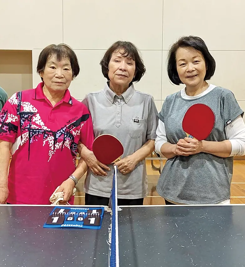 卓球仲間3名がラケットを手に笑顔で並ぶ交流の様子
