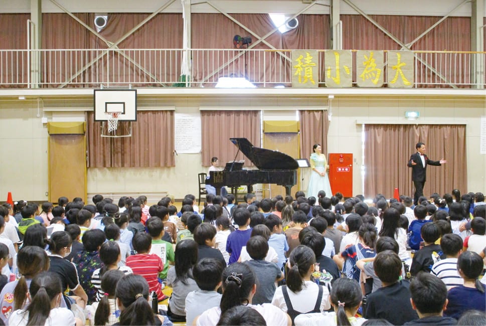 空調の効いた体育館に集まり、グランドピアノの伴奏で声楽を楽しむ大勢の児童