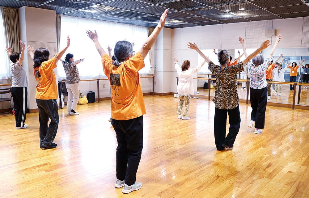 体育館でおだわら百彩の体操をする参加者たち。両腕を上げたポーズ
