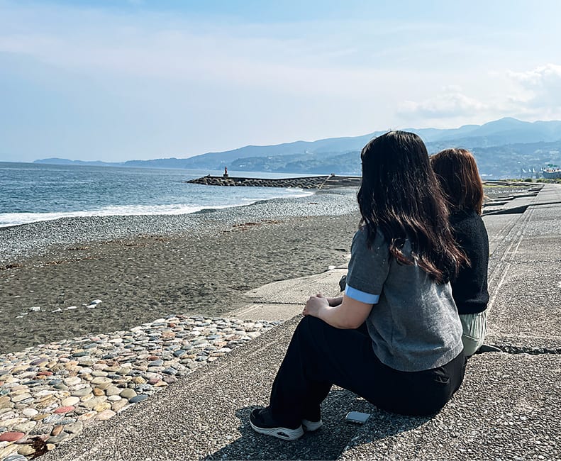 御幸の浜の砂浜に座って海を眺める2人