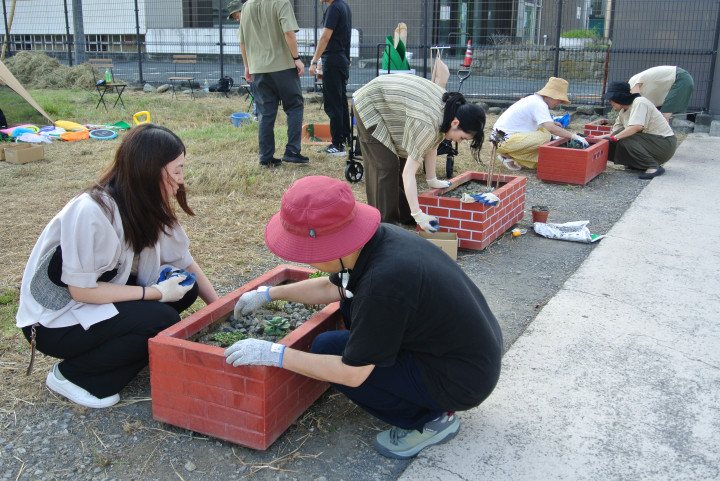 女性たちがレンガ色のプランターに多肉植物を植え、拾った石を入れ込んでいる様子。