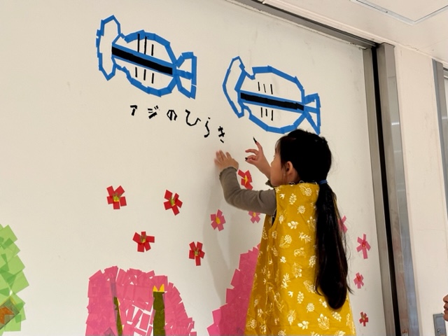 女の子がアジの開きを水色のテープで貼って作っている