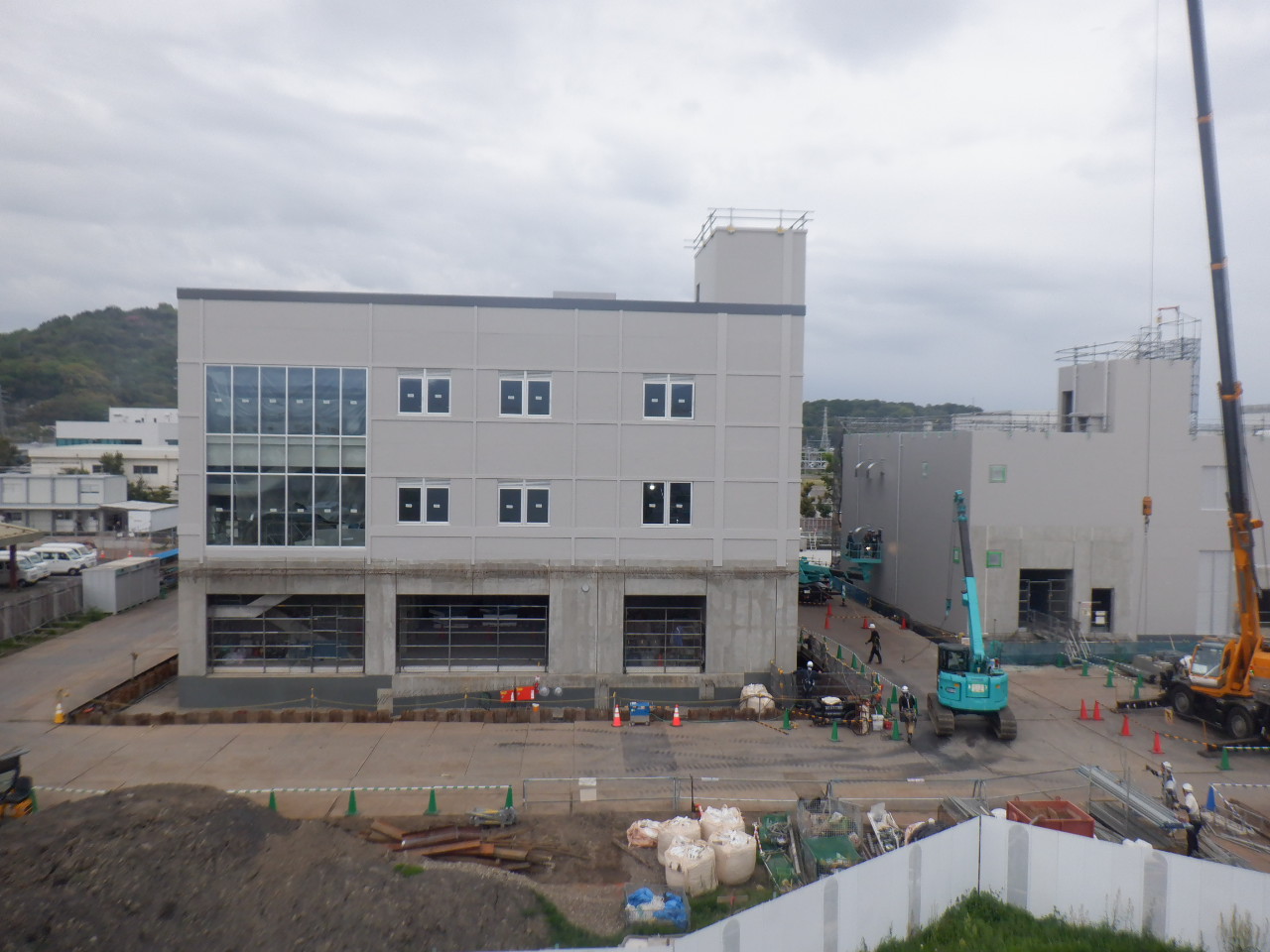写真は管理・膜ろ過棟（左側）について、コンクリート打設工事が完了し、建物が上棟しました。上棟後、西側の足場（画面手前側）を解体したことで窓ガラスの取り付けしたことが分かりやすくなりました。